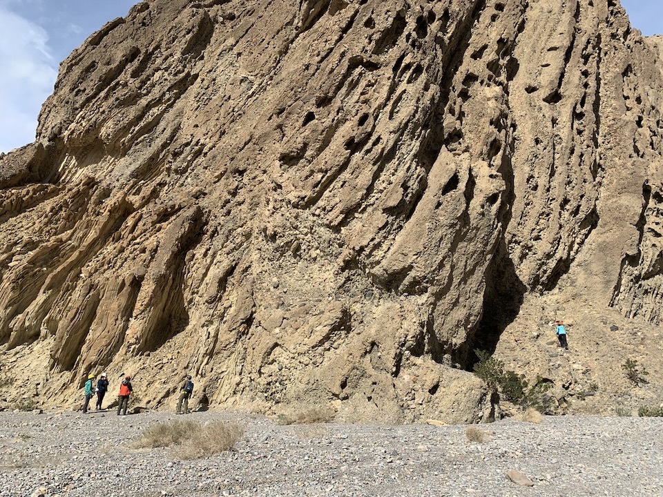 Geologists wearing green, black, red, brown, and teal jackets measuring steeply dipping, gravelly sedimentary rocks in Death Valley